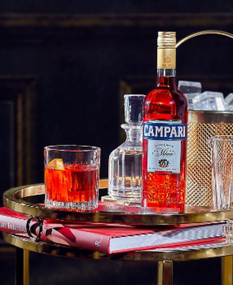 A bottle of Campari and a Negroni cocktail on a bar cart